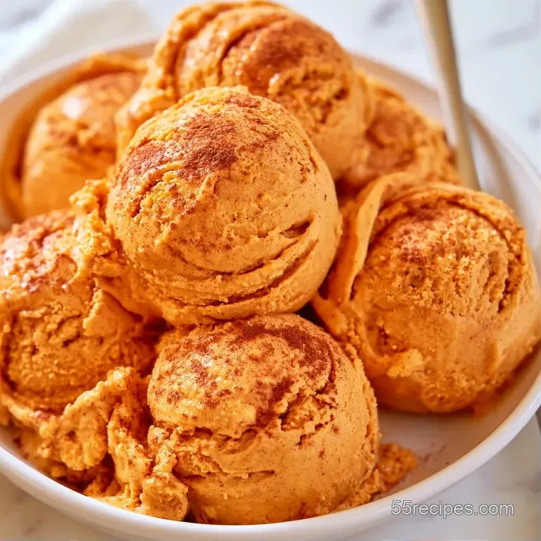 Two scoops of orange-hued frozen dessert in a glass bowl with a toasted wafer and a dusting of warm cinnamon.